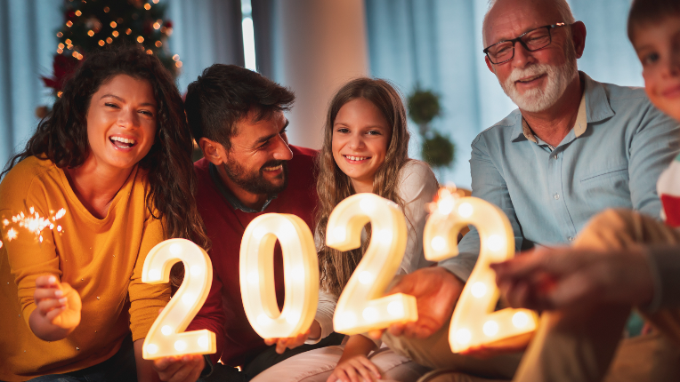 Family sitting together in home holding sparklers and light-up numbers that read “2022”